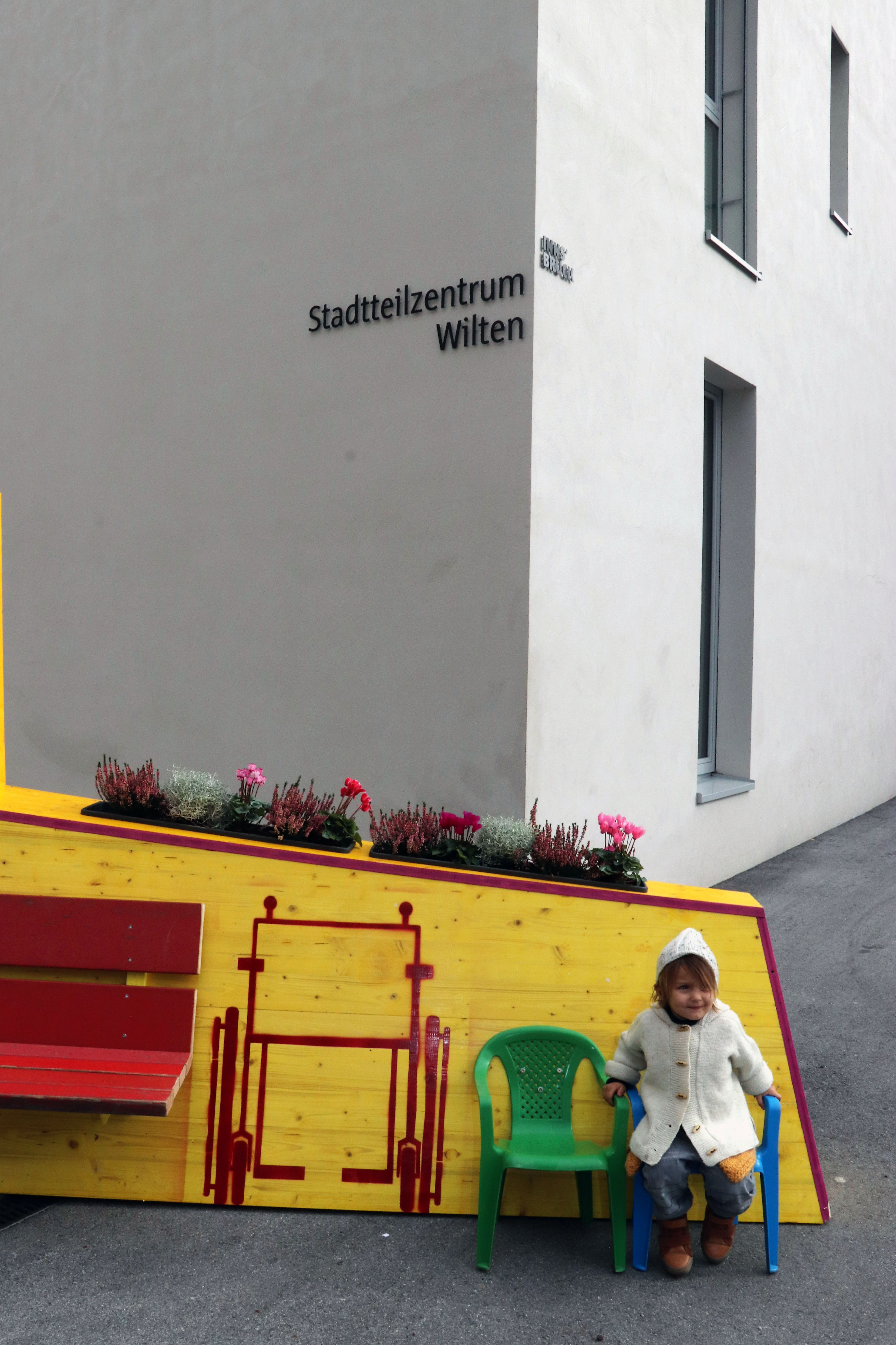 Kreativ, bunt und unübersehbar – so präsentiert sich seit 4. Oktober das temporäre, öffentliche Möbelstück vor dem Stadtteilzentrum Wilten in der Leopoldstraße 33a. Die Idee für das hölzerne Bauwerk entstand im Rahmen eines Beteiligungsprozesses bereits im Dezember 2017. Damals kamen NachbarInnen, ein Kreativteam aus Wilten und VertreterInnen des Stadtteilzentrums zusammen, um über die Gestaltung des Innenhofes zu beratschlagen. Die nun realisierte Konstruktion enthält die gewünschten Elemente, bestehend aus Beschriftung, Informations- und Plakatflächen, einem Buchtauschregal, Sitzgelegenheiten und kann mit Blumentöpfen ausgestattet werden. Bei der Einweihung kamen viele Beteiligte und UnterstützerInnen zusammen, unter ihnen auch Gemeinderätin Janine Bex, Geschäftsführer Hubert Innerebner (Innsbrucker Sozialen Dienste, ISD), Stadtteilkoordinatorin Florence Fritz sowie das Kreativteam rund um Charly Walter und zahlreiche AnrainerInnen. Bis Juni 2021 lädt das öffentliche Möbelstück vor dem Stadtteilzentrum Wilten zum Verweilen und Verwenden ein. AA