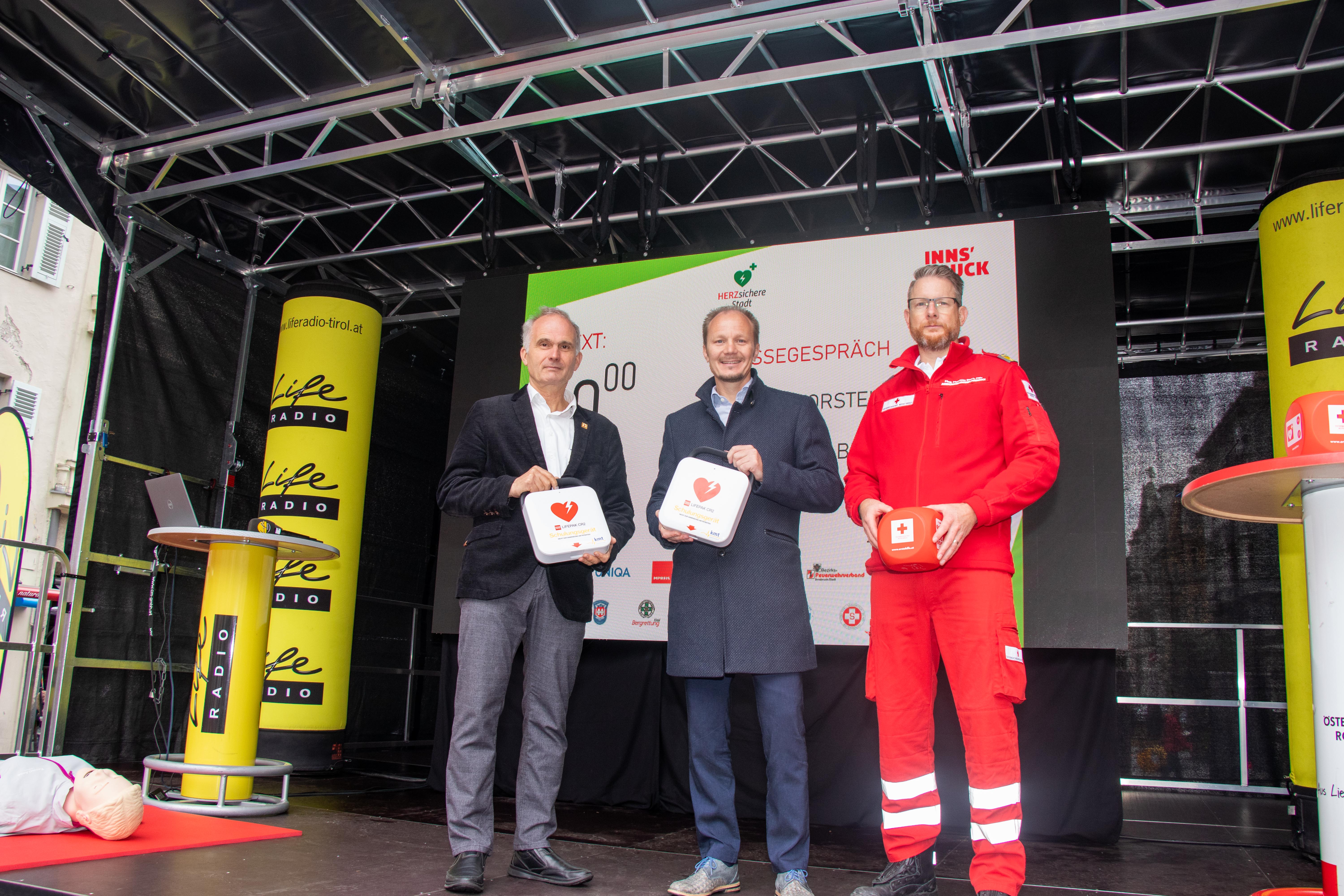 Vizebürgermeister Johannes Anzengruber, Michael Baubin, Vorsitzender des Österreichischen Rates für Wiederbelebung und Reanimations-Beauftragter für den RD des Landes Tirol (l.) sowie Matthias Stark, Leiter des Ausbildungszentrums beim Roten Kreuz Innsbruck (r.), machten beim Sicherheits- und Familienfest in der Innsbrucker Innenstadt auf die Wichtigkeit von Wiederbelebungsmaßnahmen mittels Defibrillator-Einsatz aufmerksam.