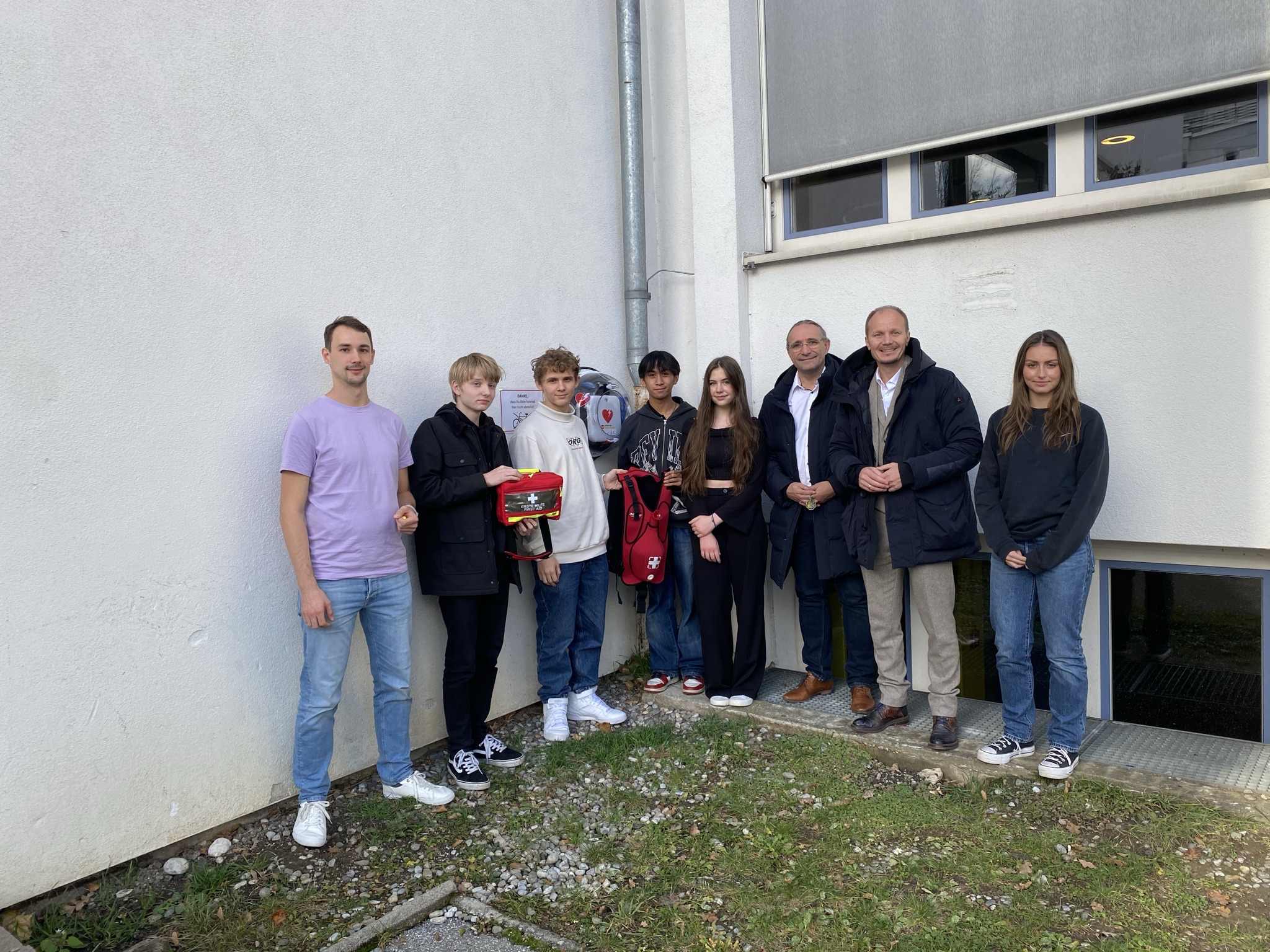 Vizebürgermeister Johannes Anzengruber (2.v.r.), Schuldirektor Walter Nigg (3.v.r.) und Lehrer bzw. Ausbildner Christoph Moser (l.) mit dem SchülerInnen-Emergency-Team und dem neuen Erste-Hilfe- vor dem Defibrillator am Reithmanngymnasium.