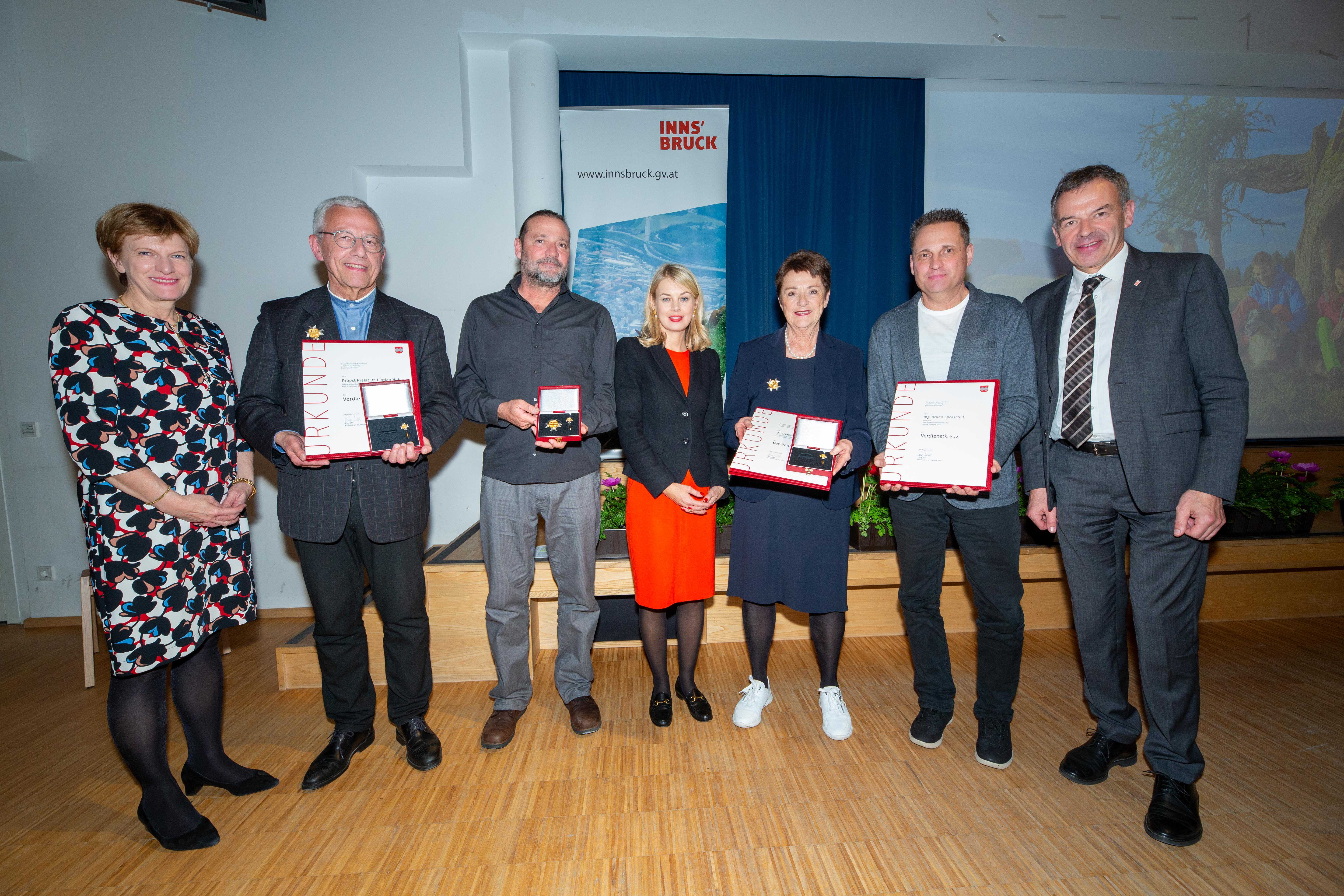 Stadträtin Christine Oppitz-Plörer (l.), Stadträtin Elisabeth Mayr (4.v.l.) und Bürgermeister Georg Willi (r.) verliehen das Verdienstkreuz der Stadt Innsbruck an Propst Florian Huber (2.v.l.), Marie-Luise Pokorny-Reitter (3.v.r.) und Bruno Sporschill (posthum, entgegengenommen von Andreas Sporschill, 3.v.l., und Heinz Sporschill, 2.v.r.).