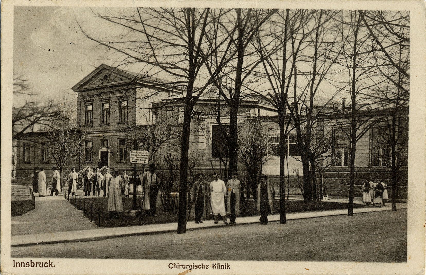 Auf dieser schwarz-weiß Postkarte ist die Chirurgische Klinik in Innsbruck abgebildet. Zahlreiche Personen posieren vor dem Gebäude für einen unbekannten Fotografen. Die Karte wurde im Jahr 1927 versendet.