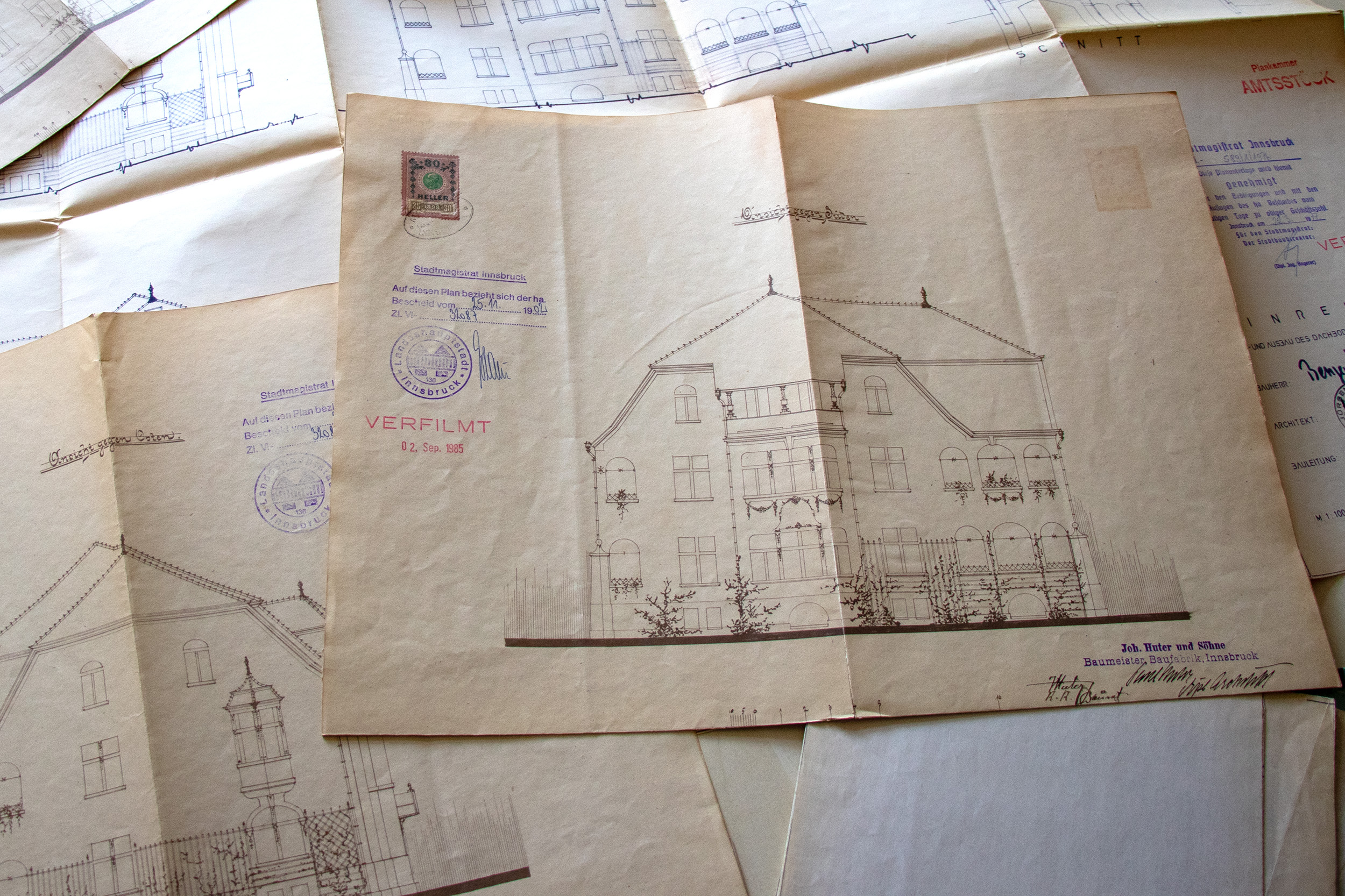 Ein Stück Innsbrucker Baugeschichte wurde heute im Amt Bau- und Feuerpolizei lebendig: Dem 94-jährigen Norbert Benzer wurden gemeinsam mit seiner Tochter Andrea Duplikate der historischen Bestandspläne seines Wohnhauses aus dem Jahr 1902 überreicht – gefertigt von der bis heute bestehenden Firma Huter & Söhne. Der rüstige Innsbrucker, der 1931 genau in jenem Haus in der Elisabethstraße geboren wurde, in dem er noch immer lebt, plant zum Abschluss seines Lebens eine Umbaumaßnahme im Gebäude: „Ich möchte meine Flügel noch ein wenig ausstrecken“, so Benzer mit einem Schmunzeln.
Gemeinsam mit Amtsvorstand Christian Kugler und Referent Manfred Hirsch vom Gebäude- und Wohnungsregister wurden die historischen Unterlagen eingehend studiert. Dabei hatte Herr Benzer so manche Anekdote aus fast einem Jahrhundert Hausgeschichte zu erzählen – von berühmten Untermietern bis hin zu einer einst verschwundenen Küche. Vielleicht wird man diese Geschichten bald in einem geplanten Podcast hören können, der Innsbrucker ZeitzeugInnen und ihre Erinnerungen zu Wort kommen lässt.