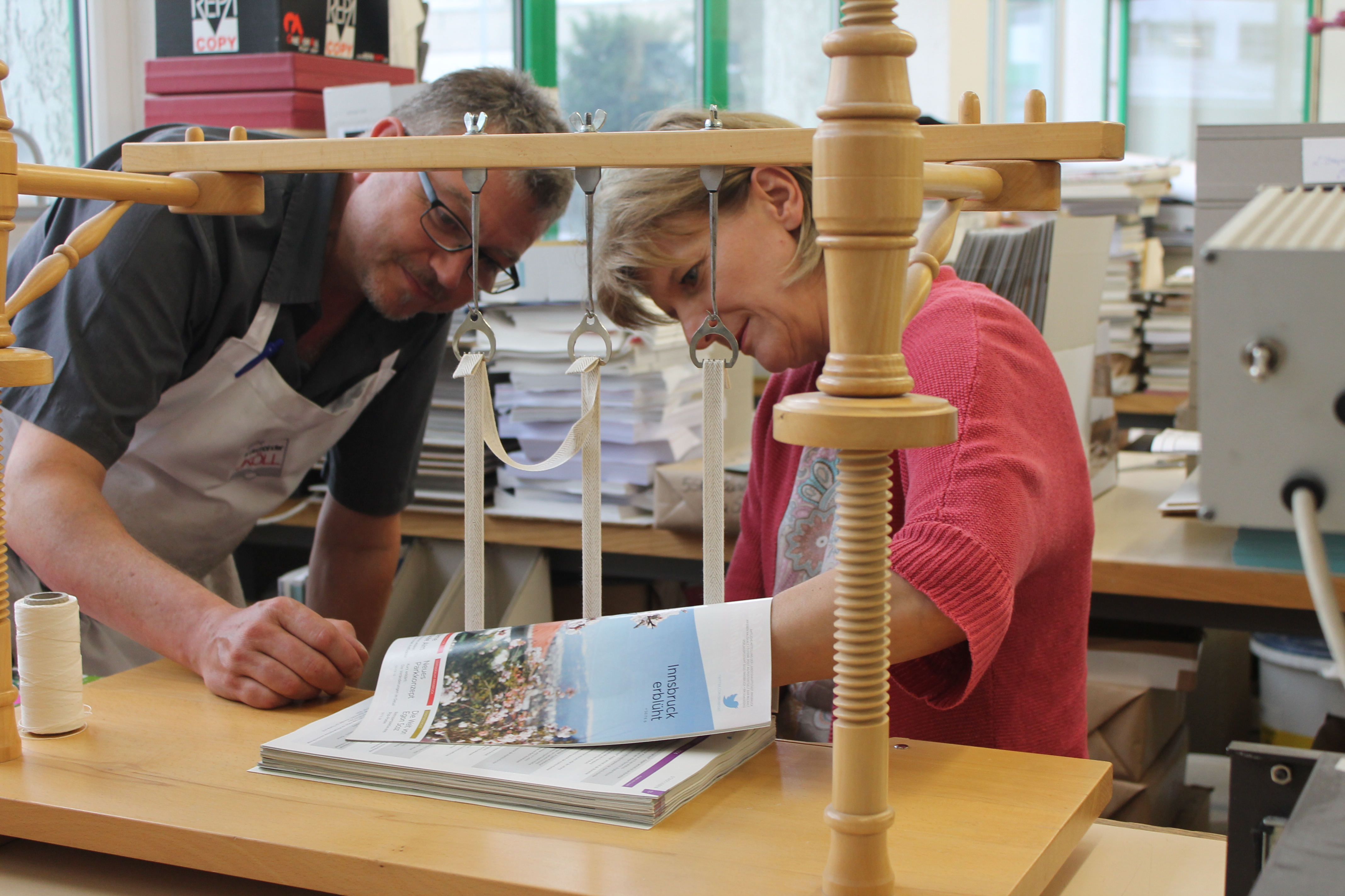 Bürgermeisterin Christine Oppitz-Plörer heftet mit Nadel und Heftfaden den gesammelten Jahrgang von „Innsbruck Informiert“ aus dem Jahre 2014 auf die Heftbänder, die auf der Heftlade aufgespannt sind. Danach erfolgt die weitere Bearbeitung des Buchblockes.