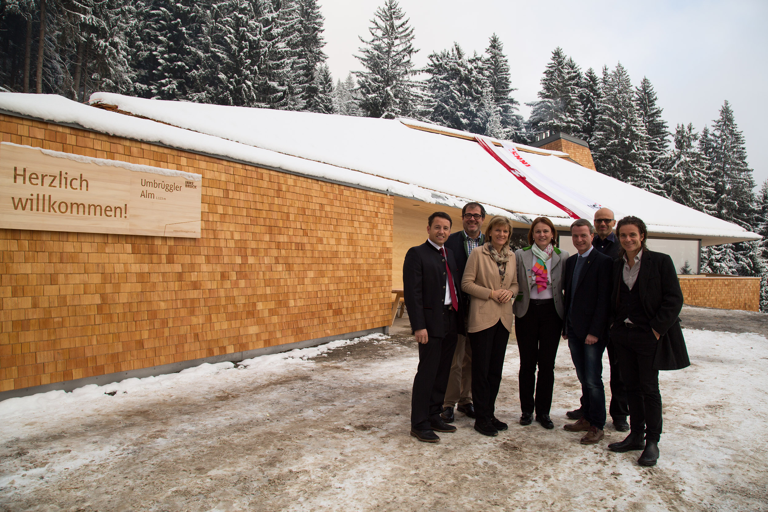 Vor der neu errichteten Umbrüggler Alm (v.l.): IIG-Geschäftsführer Franz Danler, Amtsleiter Andreas Wildauer (Land- und Forstwirtschaft), Bürgermeisterin Christine Oppitz-Plörer, Pächterin Sonja Schütz, Vizebürgermeister Christoph Kaufmann und das Architekten-Duo Philip Lutz und Elmar Ludescher.