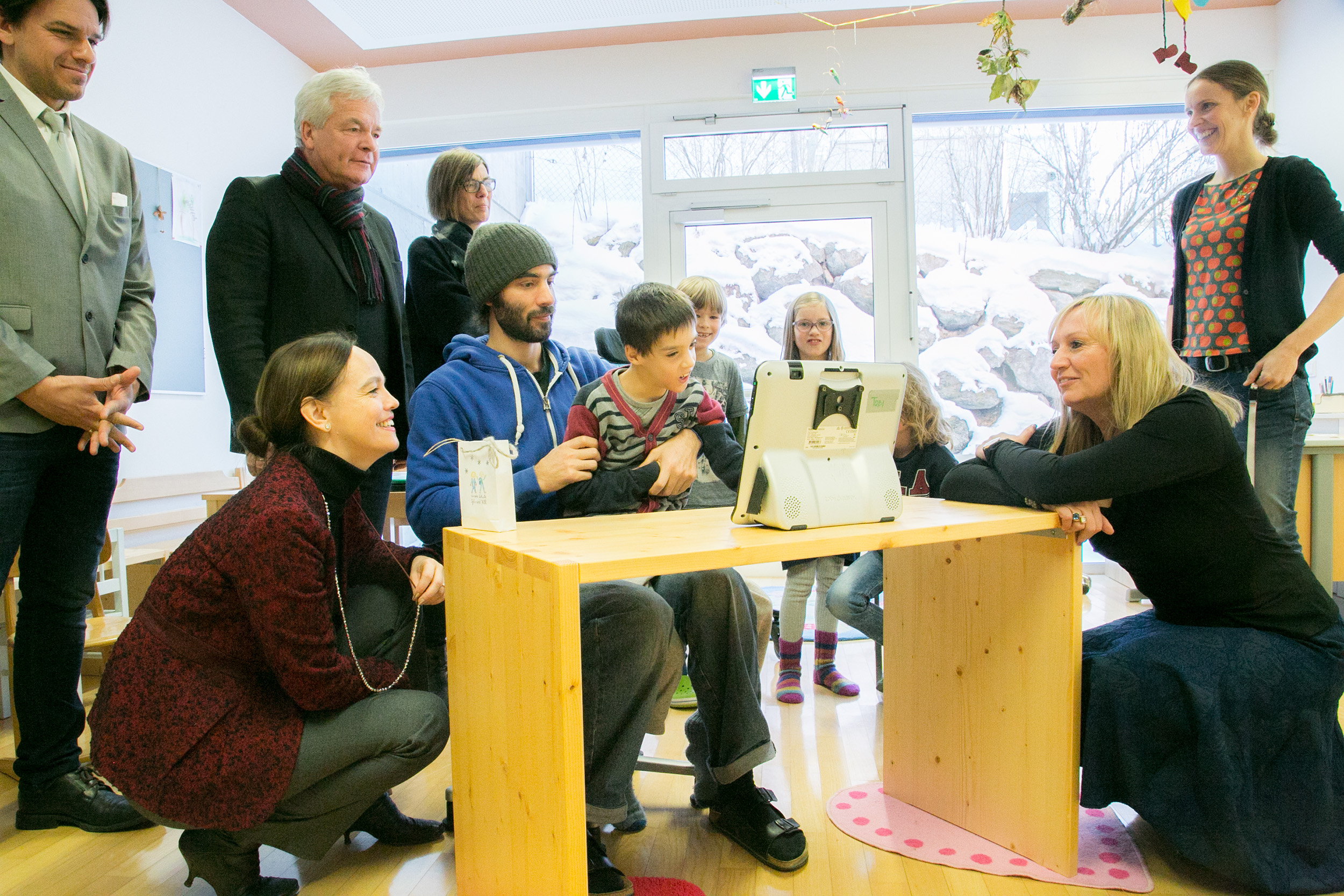 Tobi präsentiert Bildungsministerin Sonja Hammerschmid (kniend, links) und Stadtrat Ernst Pechlaner (stehend, 2.v.l.) seine Erfolge auf dem „Kommunikationsbildschirm“.
